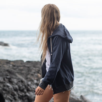 Woman wearing the recycled contrast zip hoodie by the sea, side view