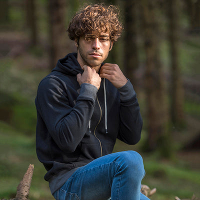 Man sitting in a forest wearing the recycled contrast zip hoodie in a dark shade