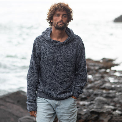 Man wearing the knitted recycled hoodie on a rocky shoreline, front view