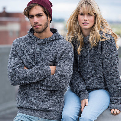 Man and woman wearing the knitted recycled hoodie outdoors, with city rooftops behind