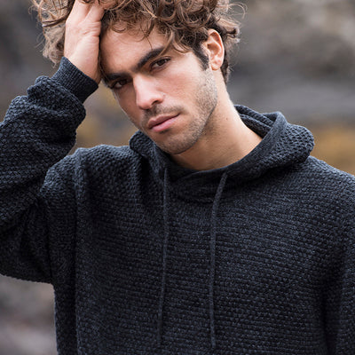 Close-up of a man wearing the knitted recycled hoodie in Charcoal/ Black, hand in his hair