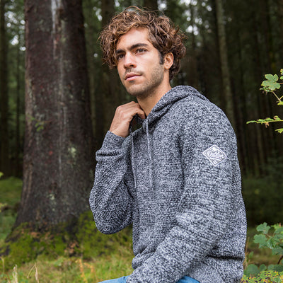 Man wearing the knitted recycled hoodie in Navy/ Heather Grey in a forest