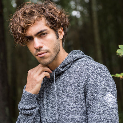 Close-up of a man wearing the knitted recycled hoodie in Navy/ Heather Grey in a forest
