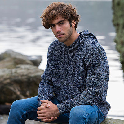 Man wearing the knitted recycled hoodie in Navy/ Heather Grey, sitting by a lake