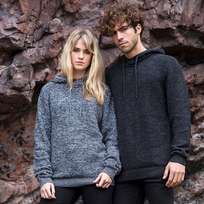 Woman in Heather/ Charcoal and man in Charcoal/ Black wearing the knitted recycled hoodie against a rock face