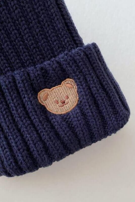 Close-up of the embroidered bear on the ribbed cuff of the knitted beanie hat in Navy