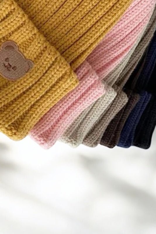 Close-up of the embroidered bear on the knitted beanie hat in Yellow, with other colours behind