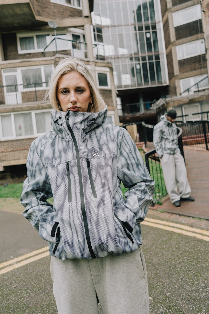 Woman wearing the waterproof windbreaker jacket in a grey and white print, zipped to the collar